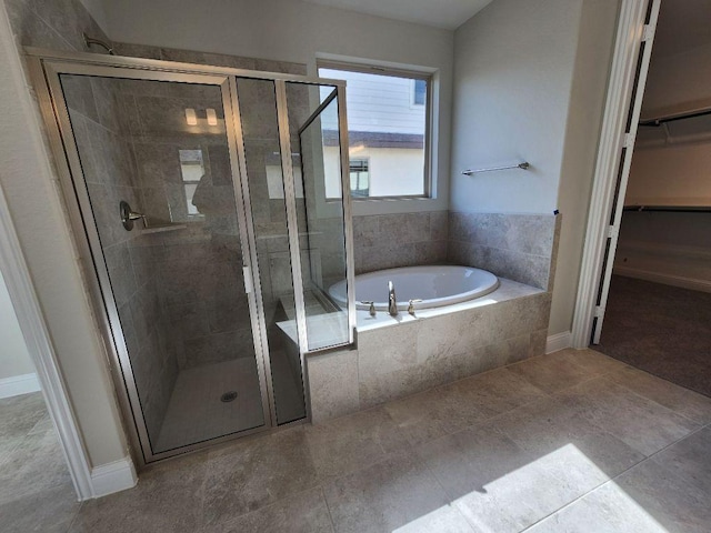 bathroom with a stall shower, a walk in closet, baseboards, and a bath