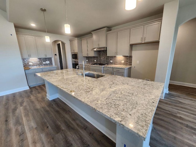 kitchen with arched walkways, a large island, appliances with stainless steel finishes, a sink, and under cabinet range hood