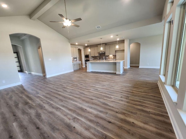 unfurnished living room with arched walkways, dark wood finished floors, visible vents, ceiling fan, and beamed ceiling