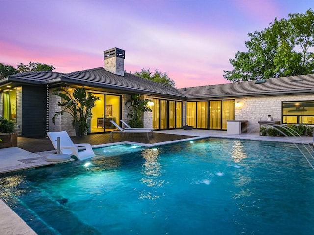 pool at dusk with pool water feature and a patio area