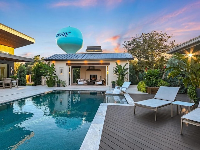 pool at dusk featuring a wooden deck, a fireplace, and a patio