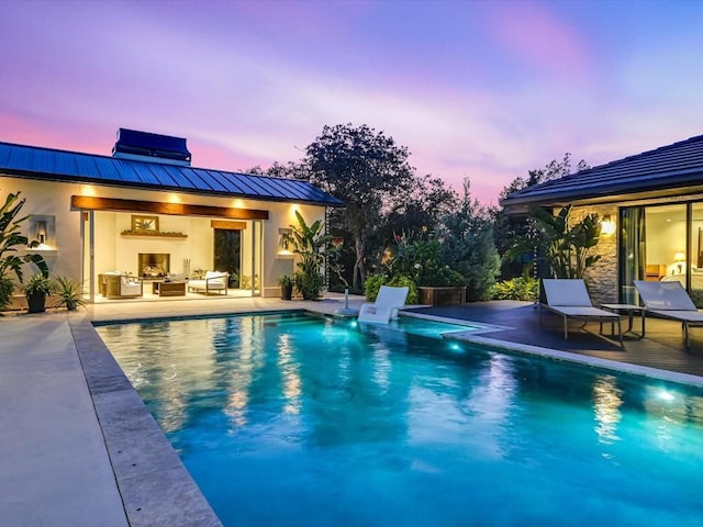 pool at dusk featuring a patio area and a fireplace