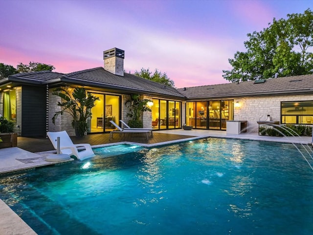 pool at dusk with pool water feature and a patio