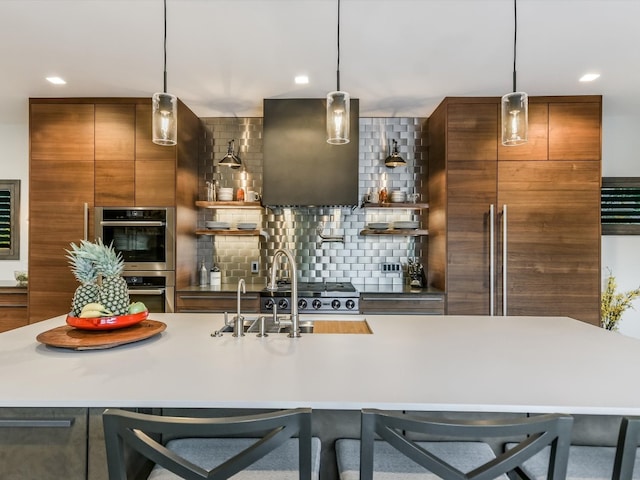 kitchen featuring backsplash, a center island with sink, hanging light fixtures, double oven, and a breakfast bar area