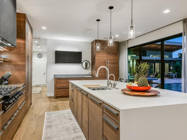 kitchen with pendant lighting, a center island with sink, sink, light hardwood / wood-style flooring, and stainless steel gas cooktop