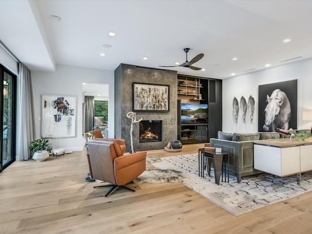 living room featuring light wood-type flooring, a large fireplace, and ceiling fan