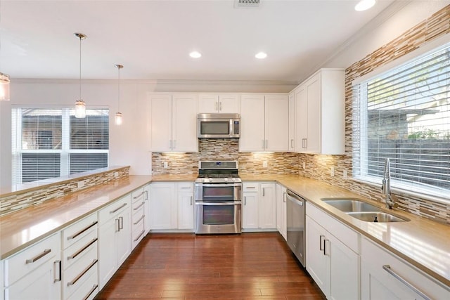 kitchen with sink, dark wood-type flooring, decorative light fixtures, white cabinets, and appliances with stainless steel finishes