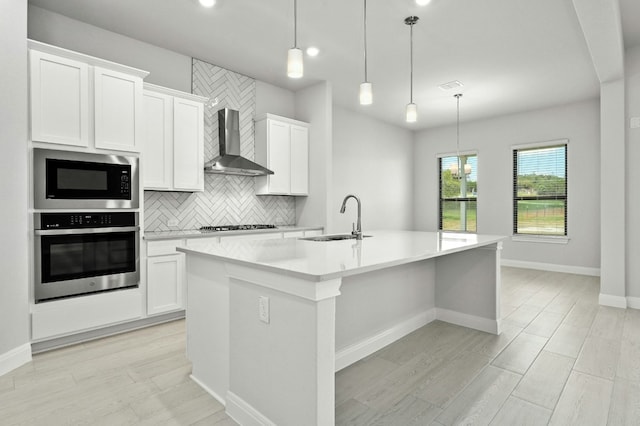 kitchen featuring stainless steel appliances, white cabinetry, a kitchen island with sink, and wall chimney exhaust hood