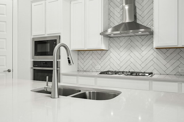 kitchen featuring black microwave, sink, wall chimney range hood, tasteful backsplash, and white cabinets