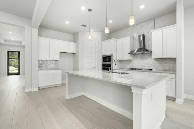 kitchen featuring white cabinetry, a kitchen island with sink, sink, and wall chimney exhaust hood