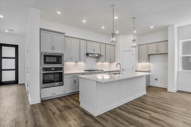 kitchen with dark wood-type flooring, sink, gray cabinetry, appliances with stainless steel finishes, and a kitchen island with sink