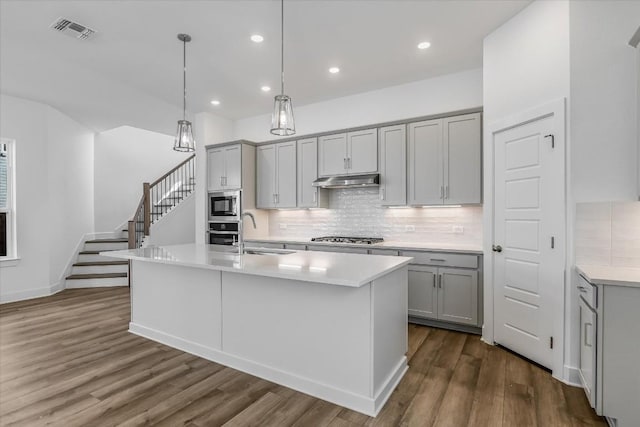 kitchen featuring sink, hanging light fixtures, appliances with stainless steel finishes, gray cabinets, and an island with sink