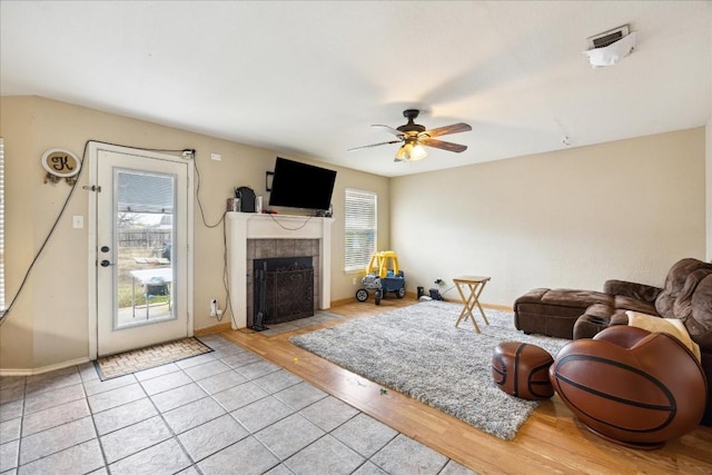 living room with a tiled fireplace, ceiling fan, and light hardwood / wood-style floors