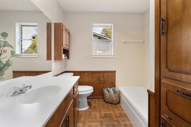 bathroom featuring parquet flooring, vanity, wooden walls, a bath, and toilet