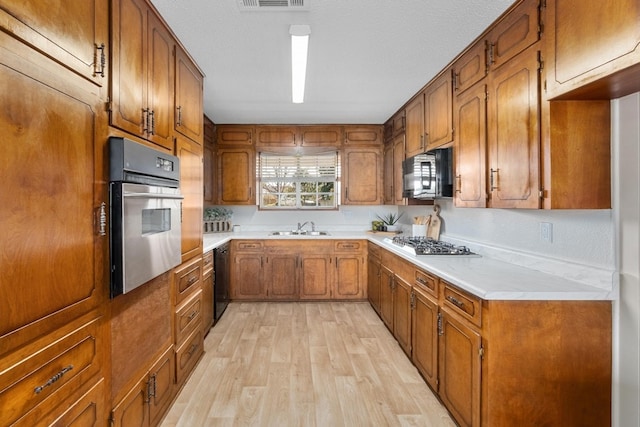 kitchen featuring black appliances, a textured ceiling, sink, and light hardwood / wood-style flooring