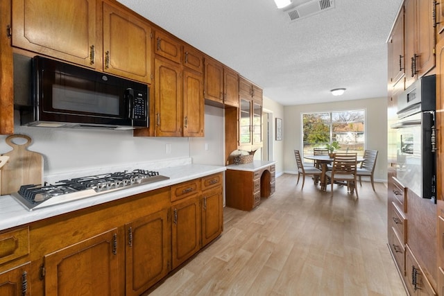 kitchen with light hardwood / wood-style flooring, black appliances, and a textured ceiling