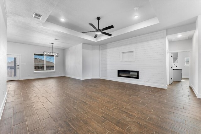 unfurnished living room with a tray ceiling, dark wood-type flooring, and ceiling fan with notable chandelier