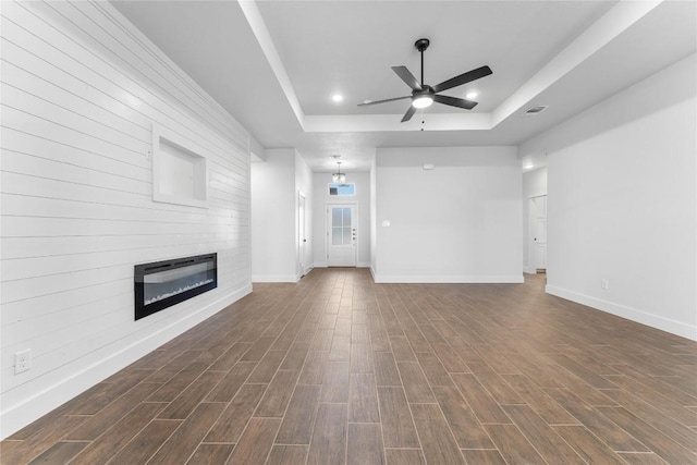 unfurnished living room featuring a raised ceiling, a large fireplace, ceiling fan with notable chandelier, and dark hardwood / wood-style floors