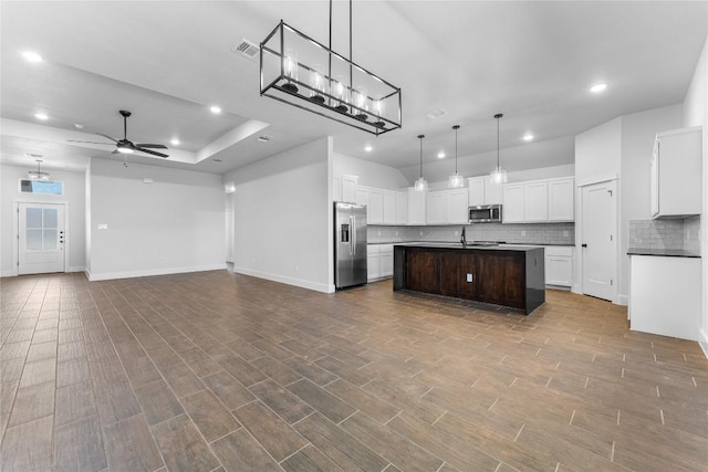 kitchen with appliances with stainless steel finishes, ceiling fan, wood-type flooring, a center island with sink, and white cabinetry