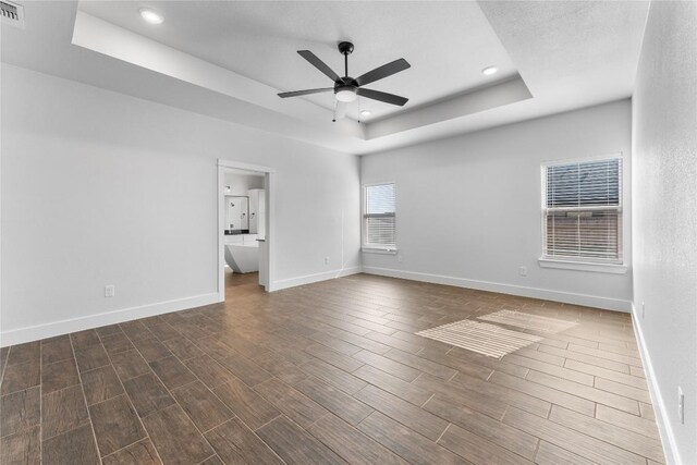 empty room with ceiling fan, dark hardwood / wood-style flooring, and a tray ceiling