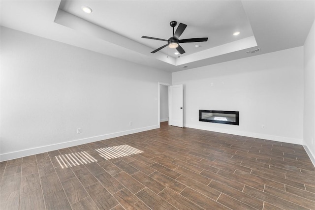 unfurnished living room featuring a tray ceiling, ceiling fan, and dark hardwood / wood-style floors