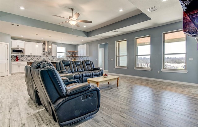 living room featuring light wood-type flooring, a raised ceiling, and ceiling fan