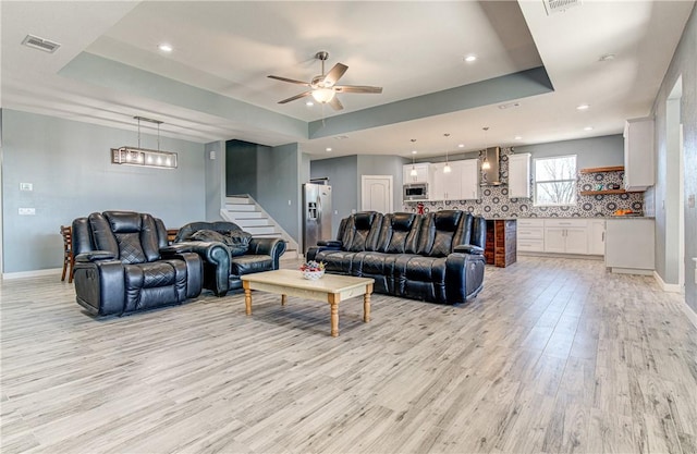 living room with ceiling fan, light hardwood / wood-style floors, and a tray ceiling