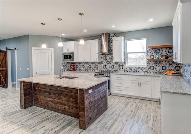 kitchen with sink, wall chimney exhaust hood, a barn door, appliances with stainless steel finishes, and white cabinetry