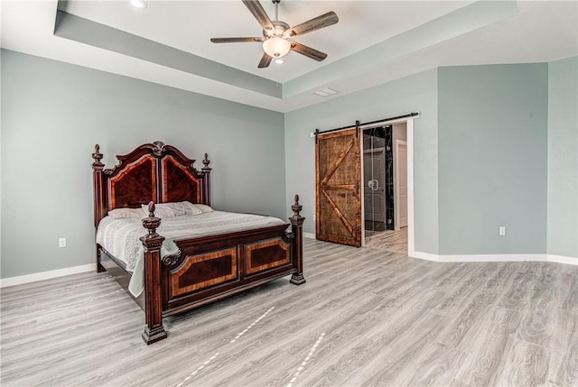 bedroom featuring ceiling fan, a barn door, a raised ceiling, and light hardwood / wood-style flooring