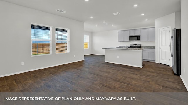 kitchen with appliances with stainless steel finishes, a center island with sink, light stone counters, and dark wood-type flooring