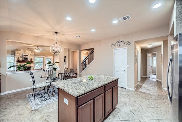 kitchen featuring light stone countertops, a center island, stainless steel fridge, decorative light fixtures, and ceiling fan with notable chandelier