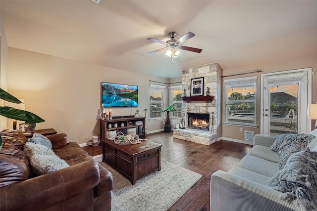 living room with dark hardwood / wood-style floors, a stone fireplace, and ceiling fan