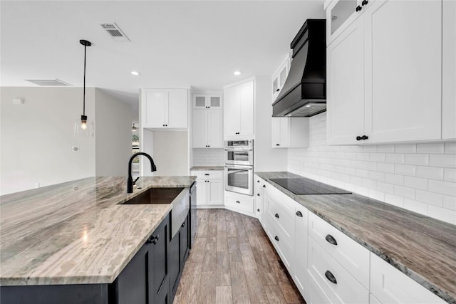 kitchen with pendant lighting, white cabinetry, light stone counters, and custom range hood