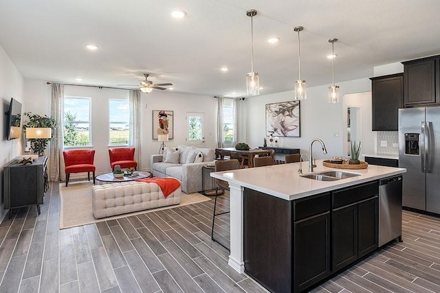 kitchen featuring pendant lighting, sink, an island with sink, appliances with stainless steel finishes, and dark hardwood / wood-style flooring