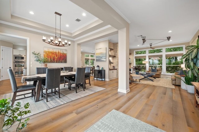 dining room featuring ceiling fan with notable chandelier, light hardwood / wood-style floors, crown molding, and a tray ceiling