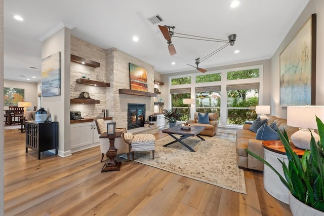 living room with ceiling fan, a fireplace, ornamental molding, and light wood-type flooring