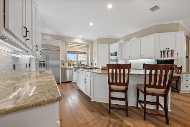 kitchen with light stone counters, built in appliances, light hardwood / wood-style flooring, a center island, and white cabinetry