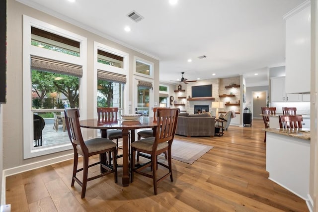 dining room featuring ceiling fan, a large fireplace, light wood-type flooring, and ornamental molding