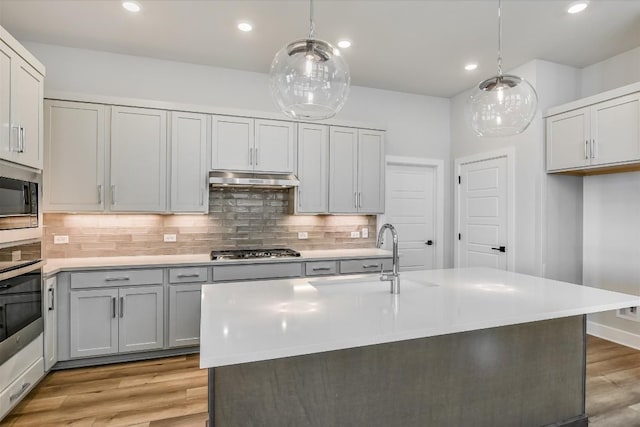 kitchen featuring sink, stainless steel appliances, decorative light fixtures, and an island with sink