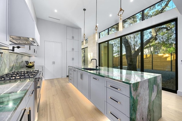 kitchen with sink, high end stainless steel range oven, pendant lighting, a kitchen island with sink, and light wood-type flooring