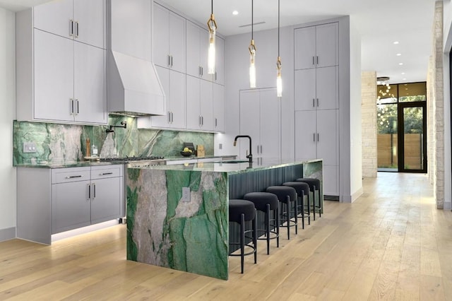 kitchen with custom exhaust hood, a spacious island, light wood-type flooring, and a breakfast bar