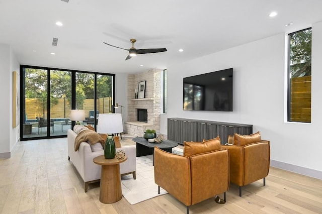 living room with ceiling fan, a fireplace, expansive windows, and light wood-type flooring