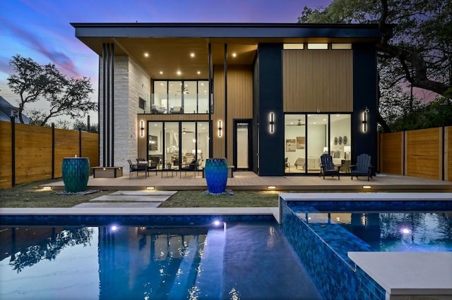 back house at dusk with pool water feature, a pool with hot tub, and a patio area