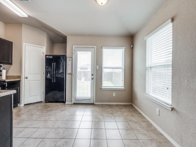 kitchen with dark brown cabinetry, black fridge with ice dispenser, light tile patterned floors, and vaulted ceiling