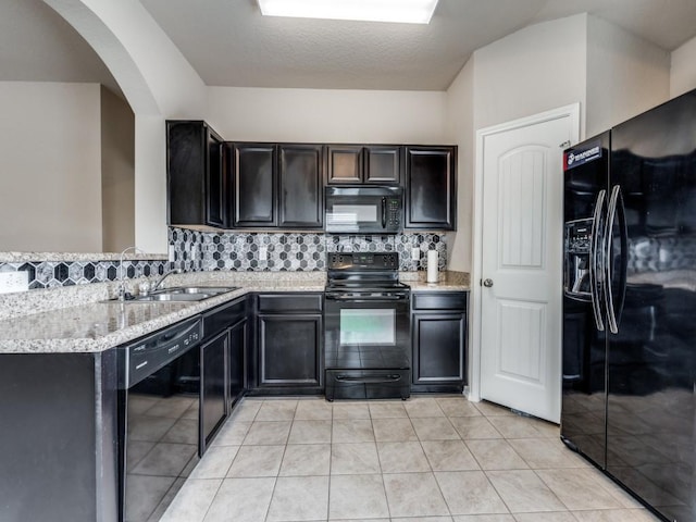 kitchen with sink, tasteful backsplash, light stone counters, light tile patterned floors, and black appliances