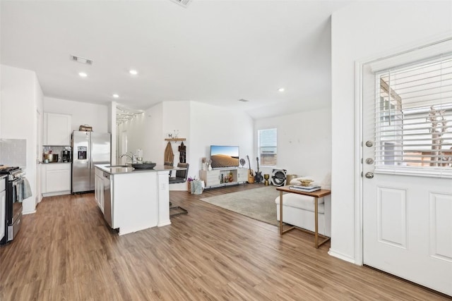 kitchen featuring appliances with stainless steel finishes, white cabinetry, a kitchen breakfast bar, a kitchen island with sink, and light wood-type flooring