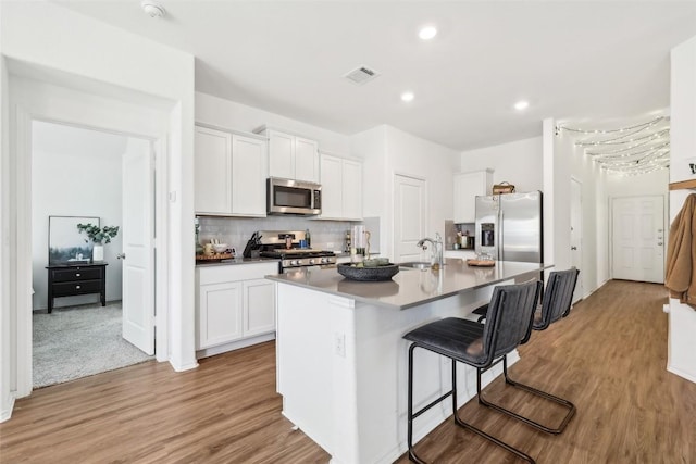 kitchen featuring a breakfast bar, light wood-type flooring, appliances with stainless steel finishes, an island with sink, and white cabinets