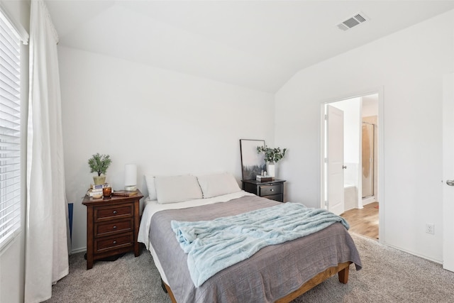 bedroom with lofted ceiling, light carpet, and ensuite bathroom