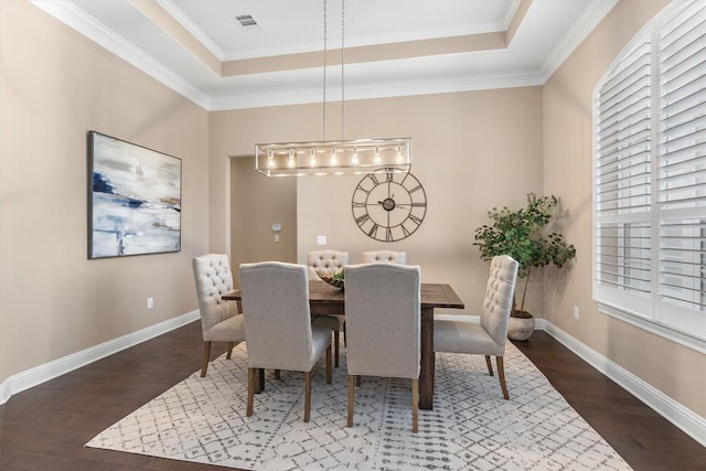 dining space with a raised ceiling, crown molding, and dark wood-type flooring