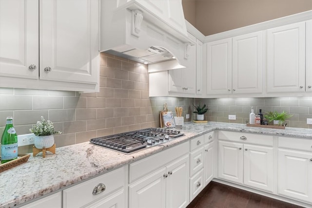 kitchen featuring decorative backsplash, premium range hood, light stone counters, stainless steel gas cooktop, and white cabinetry